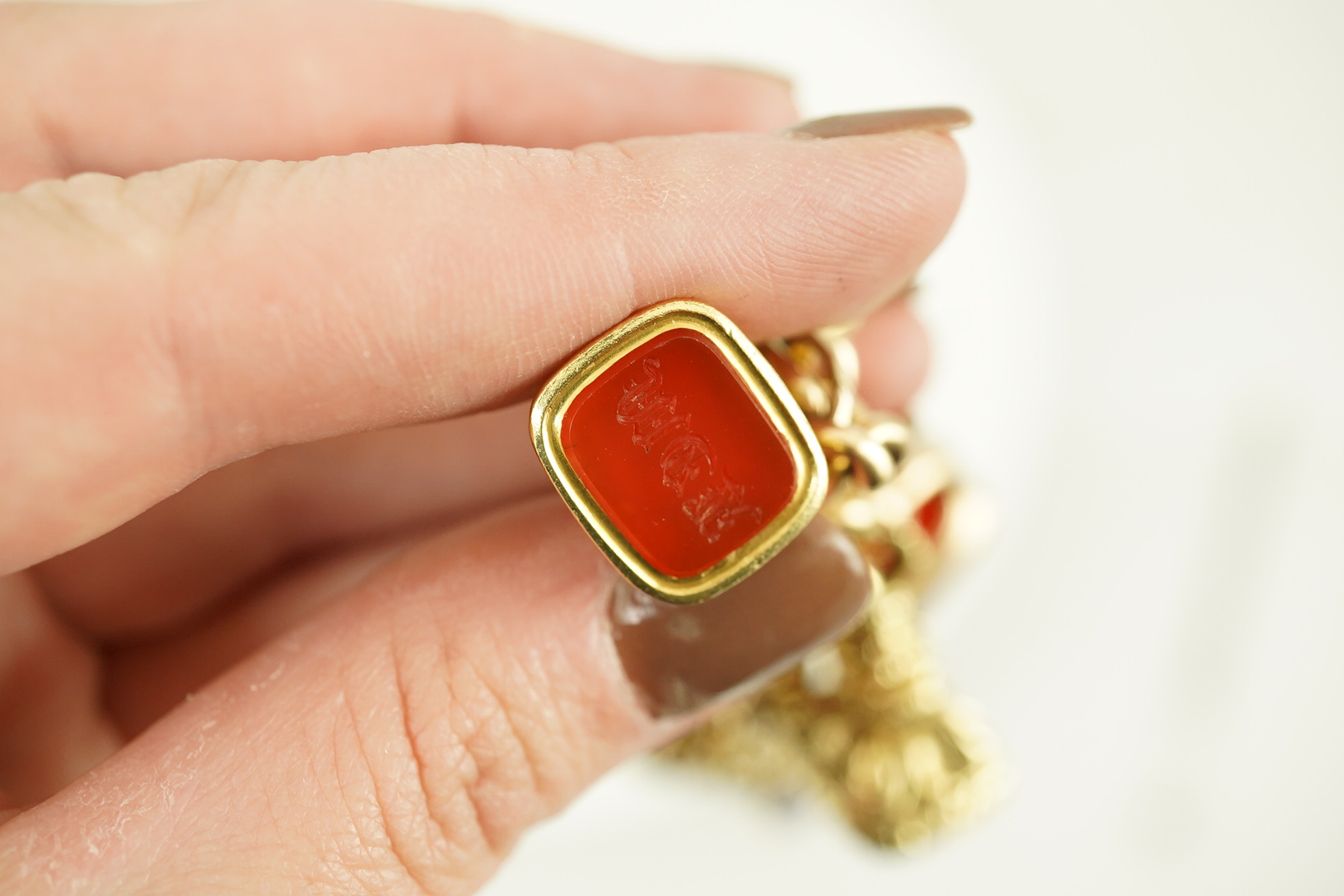 An Edwardian 15ct gold curb link charm bracelet with heart shaped padlock clasp, hung with six assorted gold overlaid and carnelian set fob seals